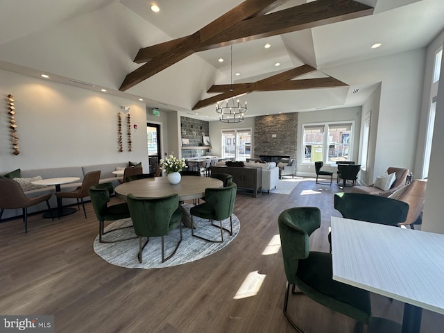 dining space featuring an inviting chandelier, hardwood / wood-style flooring, a stone fireplace, high vaulted ceiling, and beamed ceiling