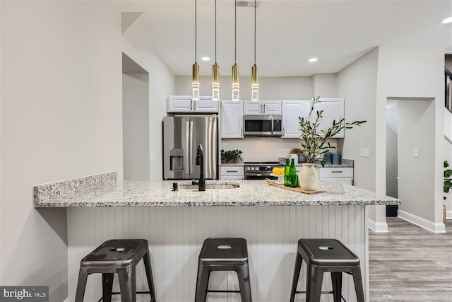 kitchen featuring a breakfast bar, sink, light stone countertops, appliances with stainless steel finishes, and white cabinetry