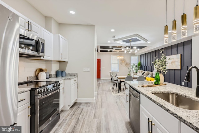 kitchen featuring light stone countertops, sink, pendant lighting, white cabinets, and appliances with stainless steel finishes