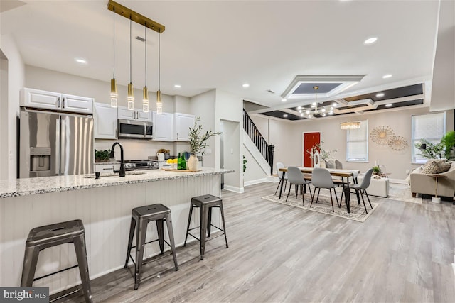 kitchen with white cabinets, appliances with stainless steel finishes, a kitchen bar, and light stone counters