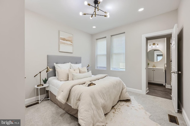 carpeted bedroom with connected bathroom and an inviting chandelier