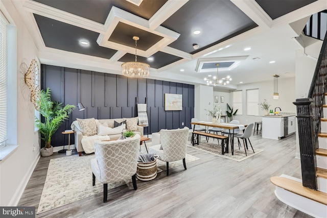 living room with a notable chandelier, light hardwood / wood-style floors, coffered ceiling, and ornamental molding