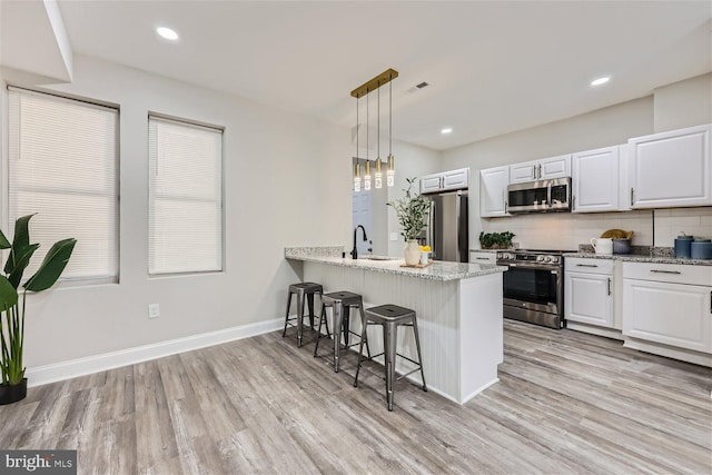 kitchen with kitchen peninsula, a kitchen breakfast bar, stainless steel appliances, pendant lighting, and white cabinets