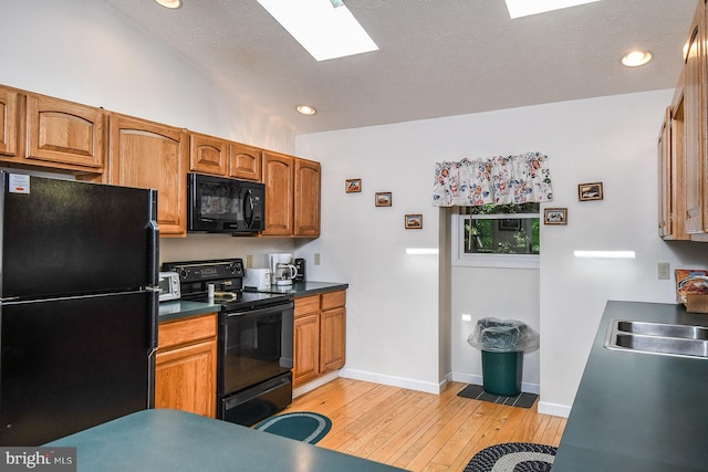 kitchen featuring black appliances, sink, a skylight, a textured ceiling, and light hardwood / wood-style floors