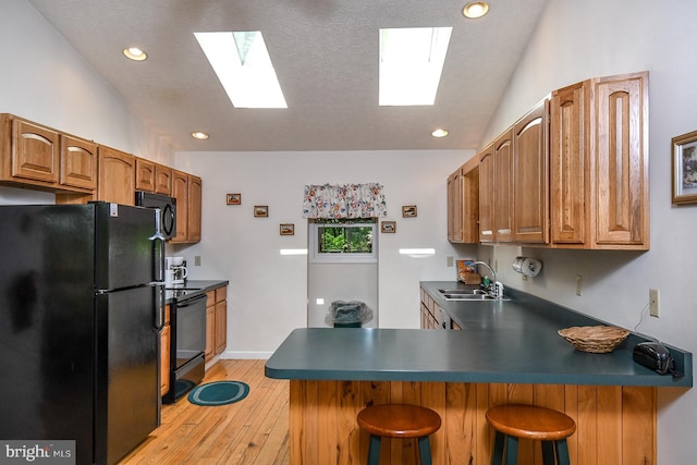 kitchen with sink, kitchen peninsula, a breakfast bar area, black appliances, and light wood-type flooring