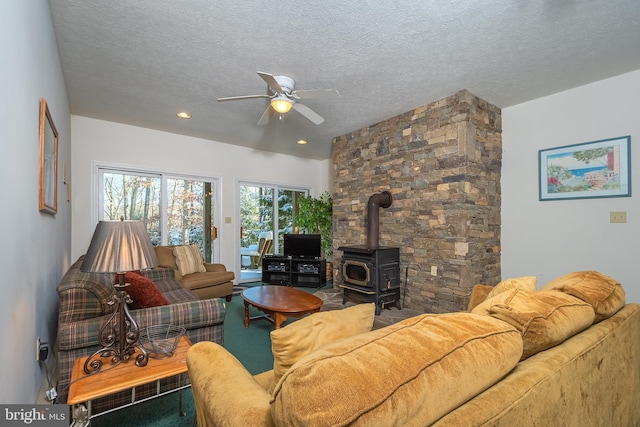 living room featuring ceiling fan, a wood stove, and a textured ceiling