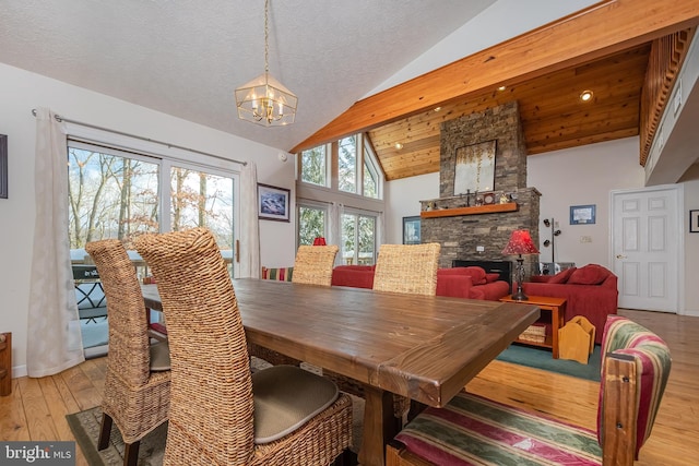 dining room with a textured ceiling, light hardwood / wood-style flooring, high vaulted ceiling, a notable chandelier, and a stone fireplace