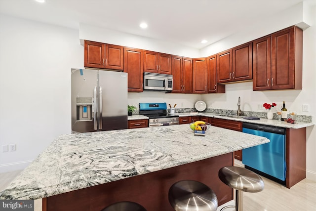 kitchen featuring sink, appliances with stainless steel finishes, a kitchen island, light stone counters, and a breakfast bar area