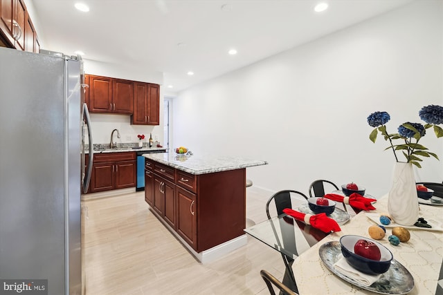 kitchen with light stone countertops, sink, a center island, light hardwood / wood-style floors, and appliances with stainless steel finishes