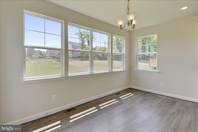 empty room featuring hardwood / wood-style floors, a notable chandelier, and a healthy amount of sunlight