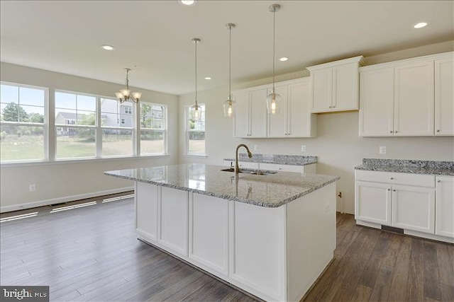 kitchen featuring light stone countertops, sink, decorative light fixtures, white cabinetry, and an island with sink