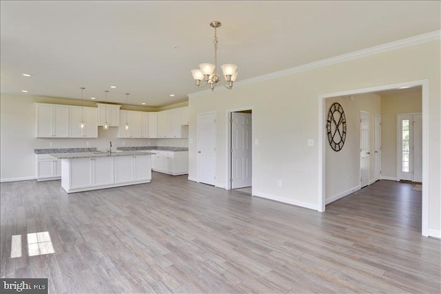 kitchen with a notable chandelier, pendant lighting, a kitchen island with sink, white cabinets, and light wood-type flooring