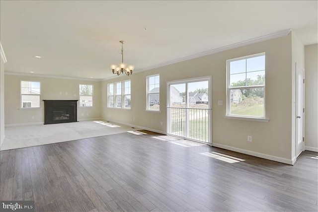 unfurnished living room featuring a healthy amount of sunlight, hardwood / wood-style flooring, ornamental molding, and a notable chandelier