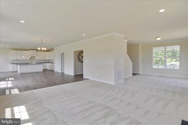 unfurnished living room featuring crown molding, light carpet, and a notable chandelier