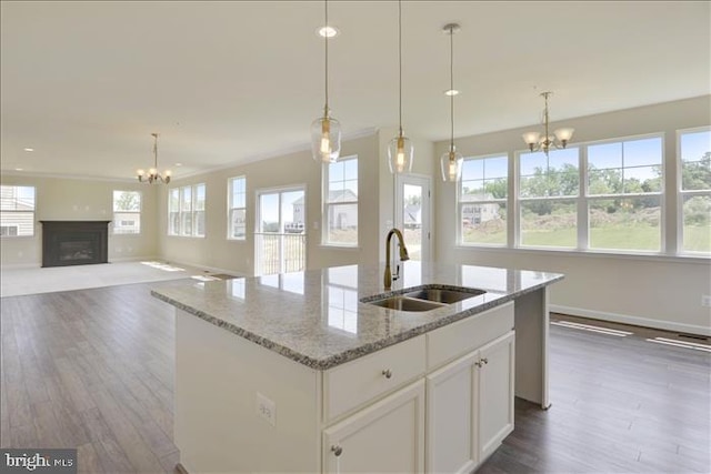 kitchen with pendant lighting, a center island with sink, white cabinets, sink, and light stone counters