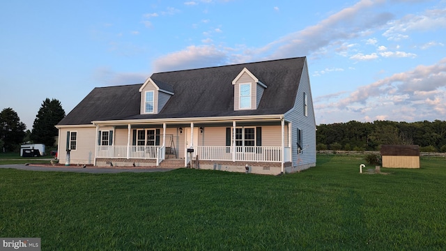 new england style home with covered porch, a front lawn, and a storage shed