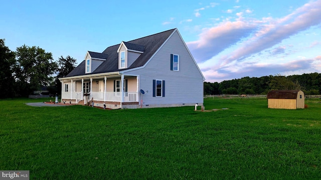 new england style home featuring a front lawn, covered porch, and a shed