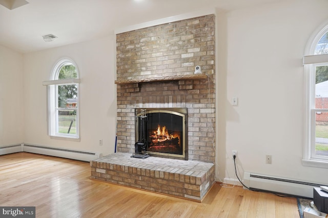 living room featuring a brick fireplace, a baseboard radiator, and light hardwood / wood-style floors