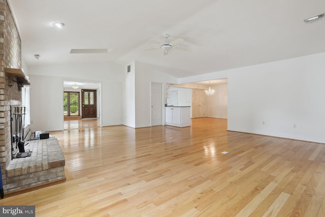 living room with a brick fireplace, ceiling fan with notable chandelier, vaulted ceiling, and light wood-type flooring