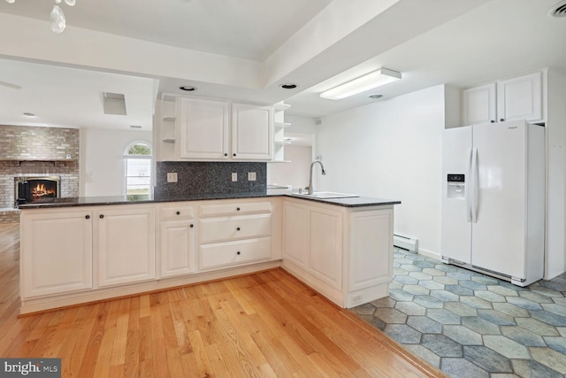 kitchen with tasteful backsplash, a baseboard radiator, sink, white refrigerator with ice dispenser, and kitchen peninsula