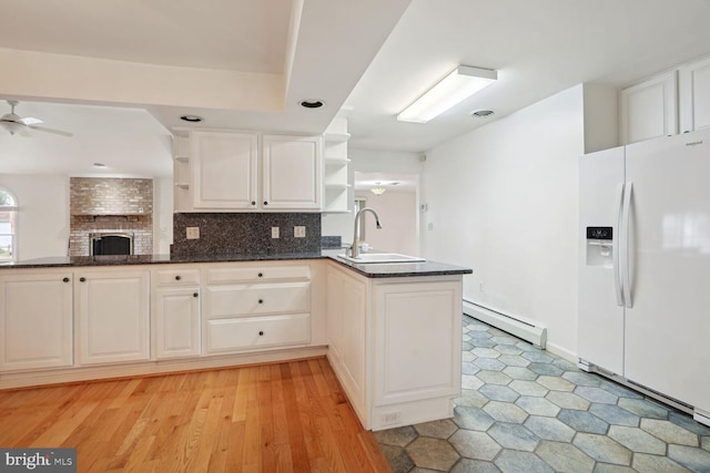 kitchen featuring ceiling fan, a baseboard heating unit, kitchen peninsula, sink, and white fridge with ice dispenser