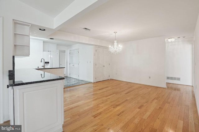 kitchen featuring white cabinetry, decorative light fixtures, a chandelier, white refrigerator with ice dispenser, and light hardwood / wood-style floors