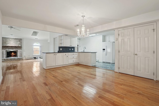 kitchen with a fireplace, white cabinetry, hanging light fixtures, white refrigerator with ice dispenser, and kitchen peninsula