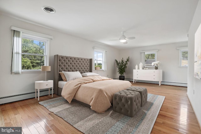 bedroom with ceiling fan, light hardwood / wood-style floors, and a baseboard heating unit