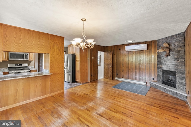 kitchen with a baseboard heating unit, a wall unit AC, an inviting chandelier, wooden walls, and stainless steel appliances