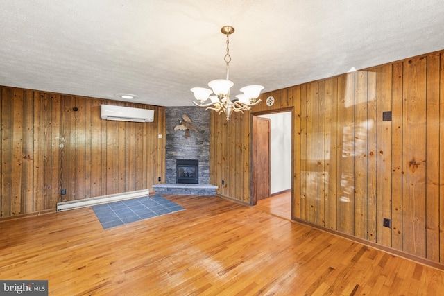 unfurnished living room with a wall mounted AC, a fireplace, an inviting chandelier, hardwood / wood-style flooring, and baseboard heating