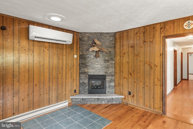 unfurnished living room with wood walls, a stone fireplace, a baseboard heating unit, a textured ceiling, and an AC wall unit