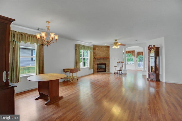 unfurnished living room featuring hardwood / wood-style floors, ceiling fan with notable chandelier, and a stone fireplace