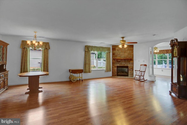 unfurnished living room featuring wood-type flooring, ceiling fan with notable chandelier, and a stone fireplace