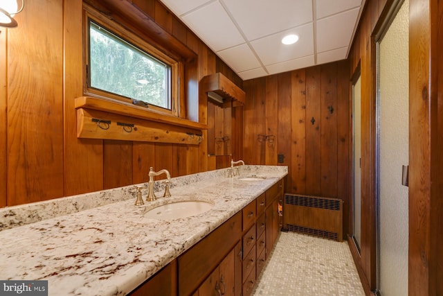 bathroom featuring tile patterned floors, a drop ceiling, vanity, radiator heating unit, and wood walls