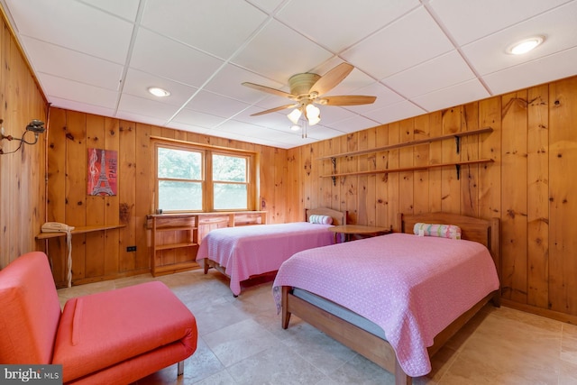 bedroom with ceiling fan, a drop ceiling, and wood walls