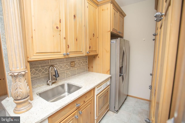 kitchen featuring stainless steel fridge, backsplash, light stone counters, and sink