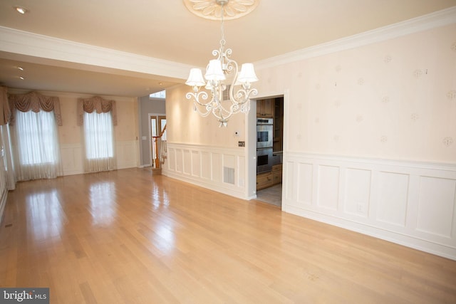 unfurnished dining area with plenty of natural light, light hardwood / wood-style floors, crown molding, and an inviting chandelier