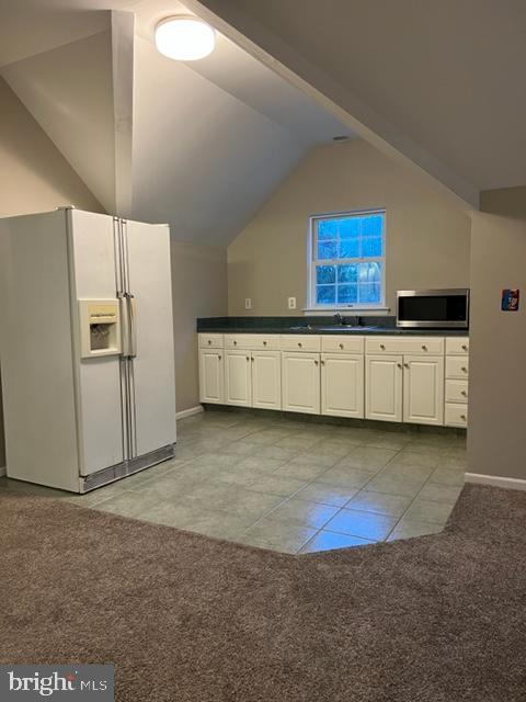 kitchen with sink, white refrigerator with ice dispenser, white cabinetry, lofted ceiling, and light tile patterned flooring