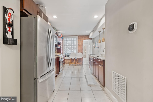 kitchen featuring hanging light fixtures, light stone countertops, appliances with stainless steel finishes, light tile patterned flooring, and brick wall