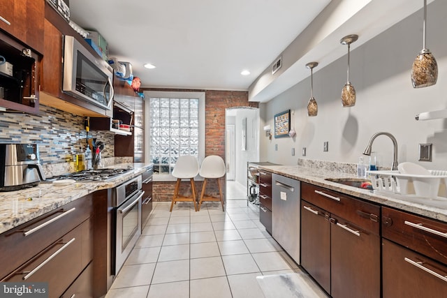 kitchen featuring appliances with stainless steel finishes, tasteful backsplash, decorative light fixtures, light tile patterned flooring, and light stone counters