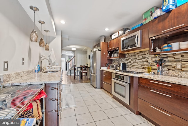 kitchen featuring pendant lighting, light stone countertops, backsplash, and appliances with stainless steel finishes