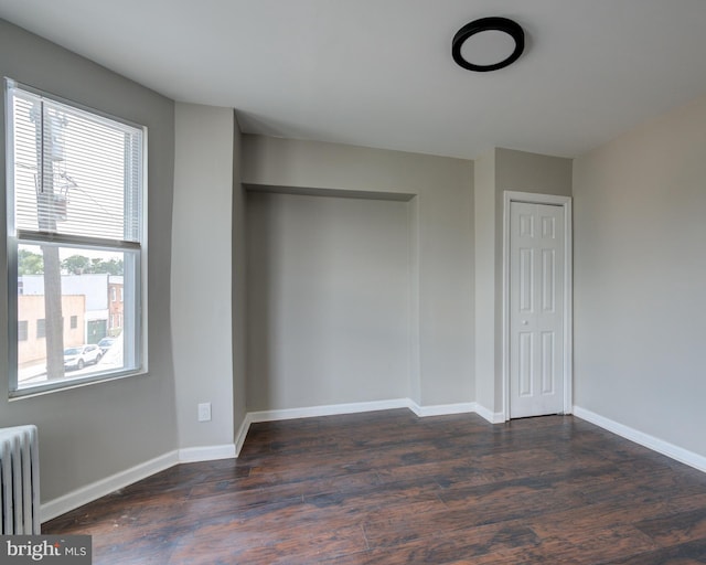 unfurnished bedroom with multiple windows, radiator heating unit, and dark wood-type flooring