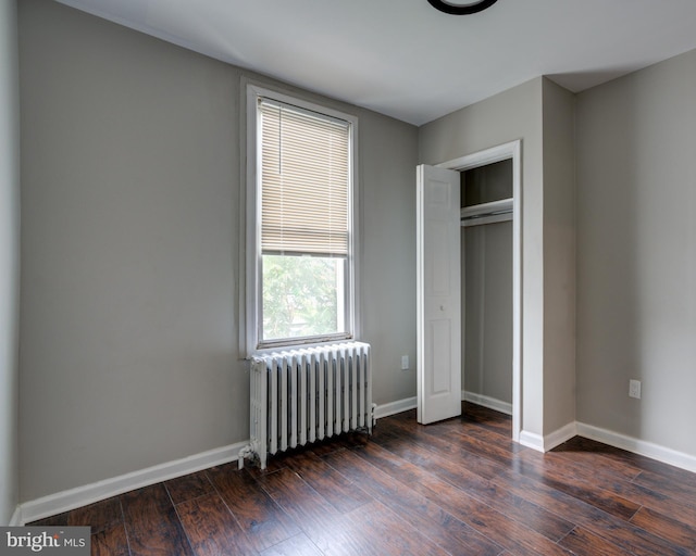 unfurnished bedroom featuring radiator, a closet, and dark hardwood / wood-style flooring