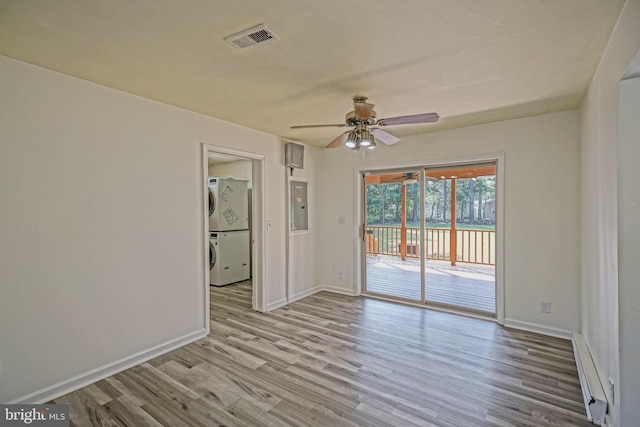 empty room with baseboard heating, stacked washer and clothes dryer, ceiling fan, electric panel, and light hardwood / wood-style flooring