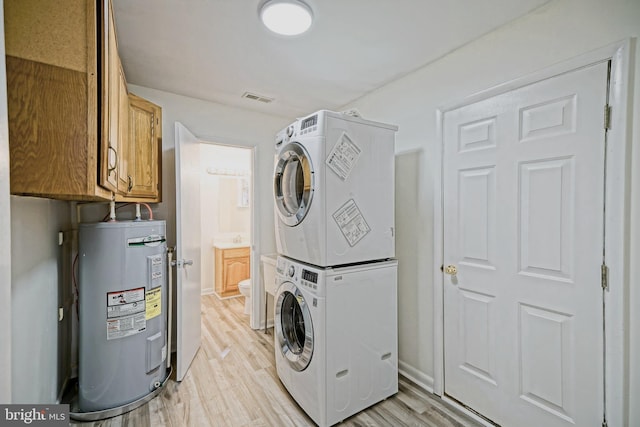 clothes washing area with light hardwood / wood-style floors, cabinets, stacked washer and clothes dryer, and water heater