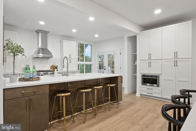 kitchen featuring light hardwood / wood-style flooring, stainless steel oven, wall chimney range hood, decorative backsplash, and sink