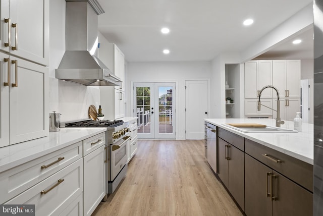 kitchen with white cabinetry, stainless steel appliances, light hardwood / wood-style floors, wall chimney exhaust hood, and sink