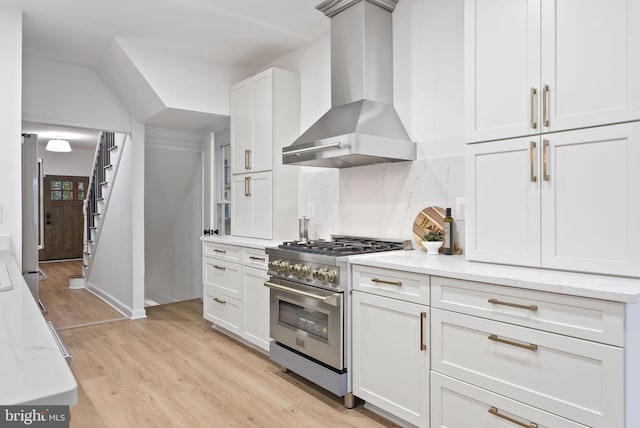 kitchen with stainless steel stove, light wood-type flooring, backsplash, light stone countertops, and wall chimney exhaust hood