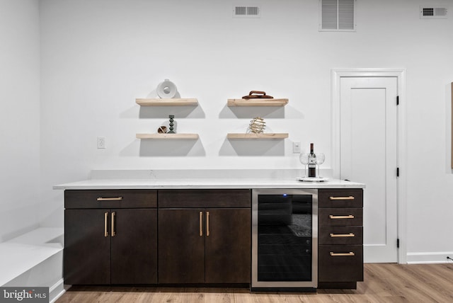 bar with light hardwood / wood-style floors, dark brown cabinetry, and beverage cooler