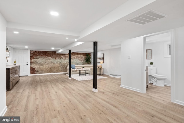 basement with brick wall and light hardwood / wood-style flooring